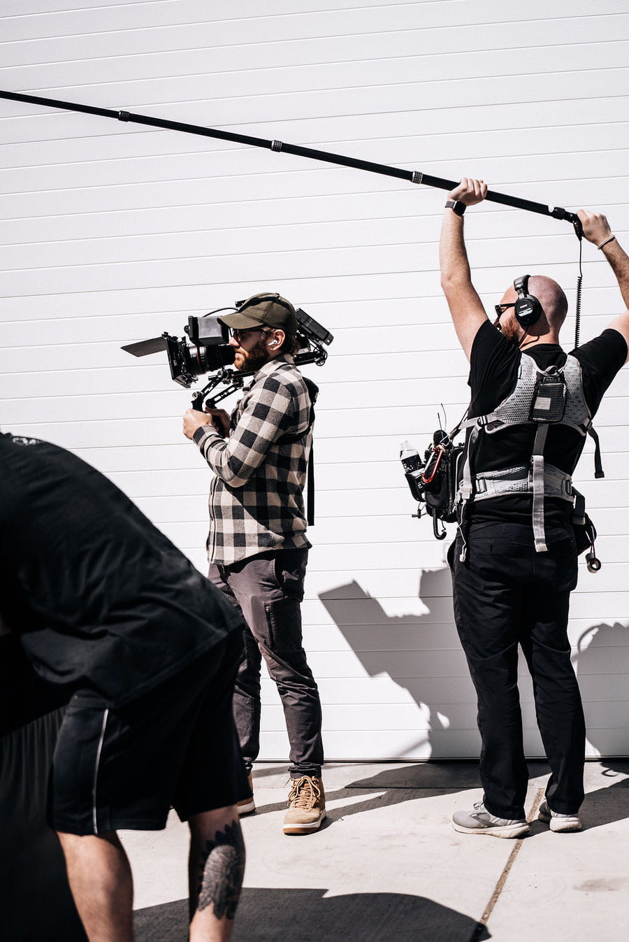 Camera operator and boom operator filming against a white garage wall