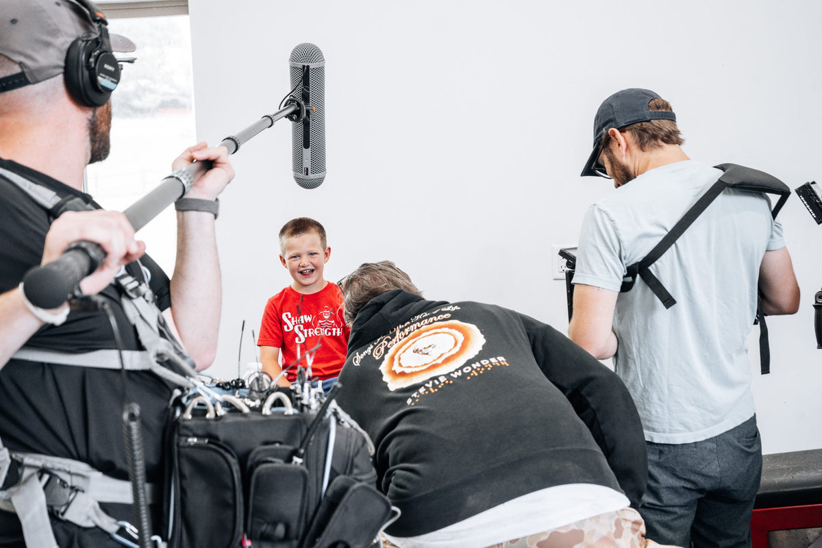 Brian's son laughs during his on-camera interview, in a red Shaw Strength shirt